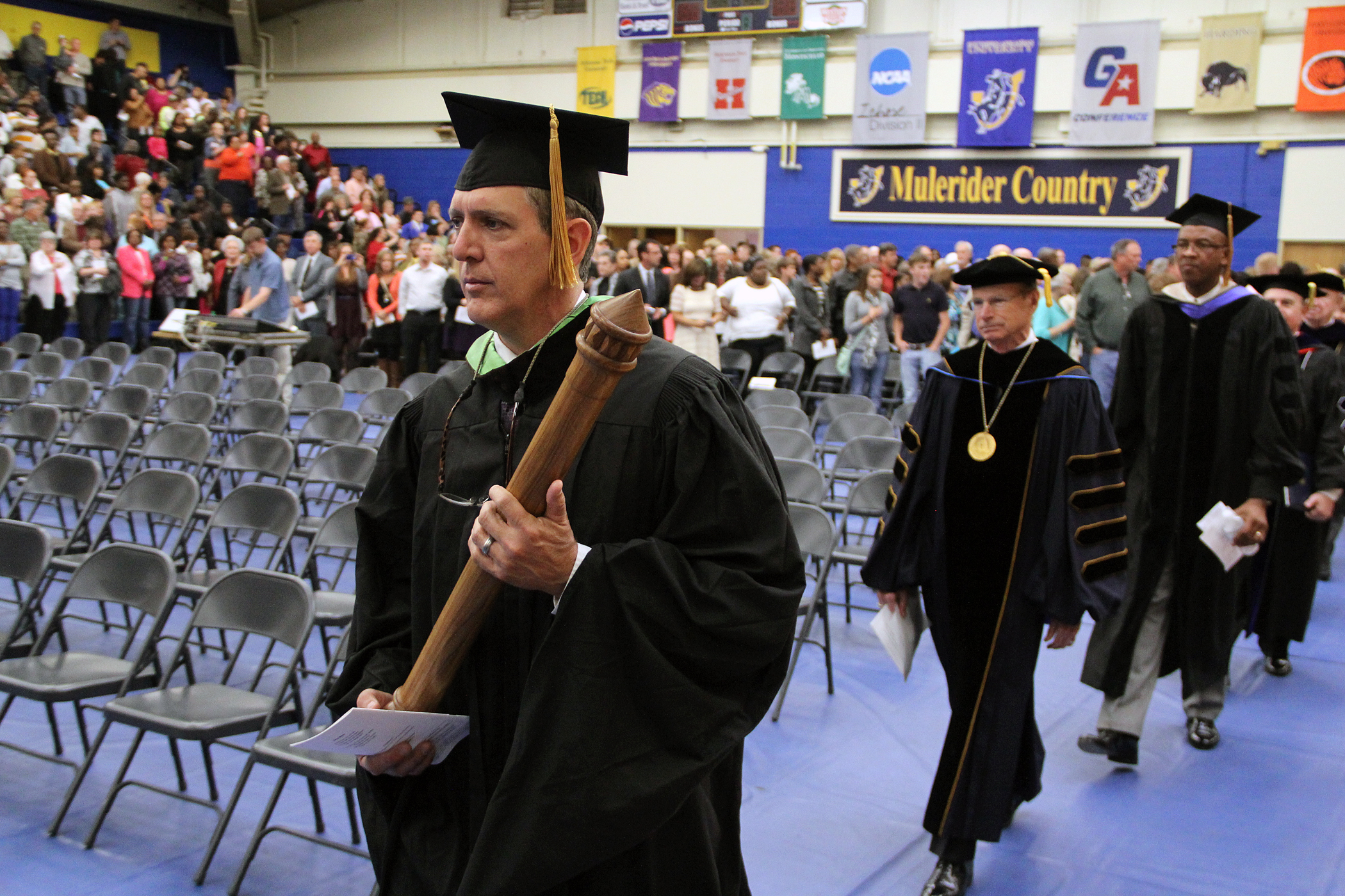 a graduate carries a large pipe during a graduation ceremony