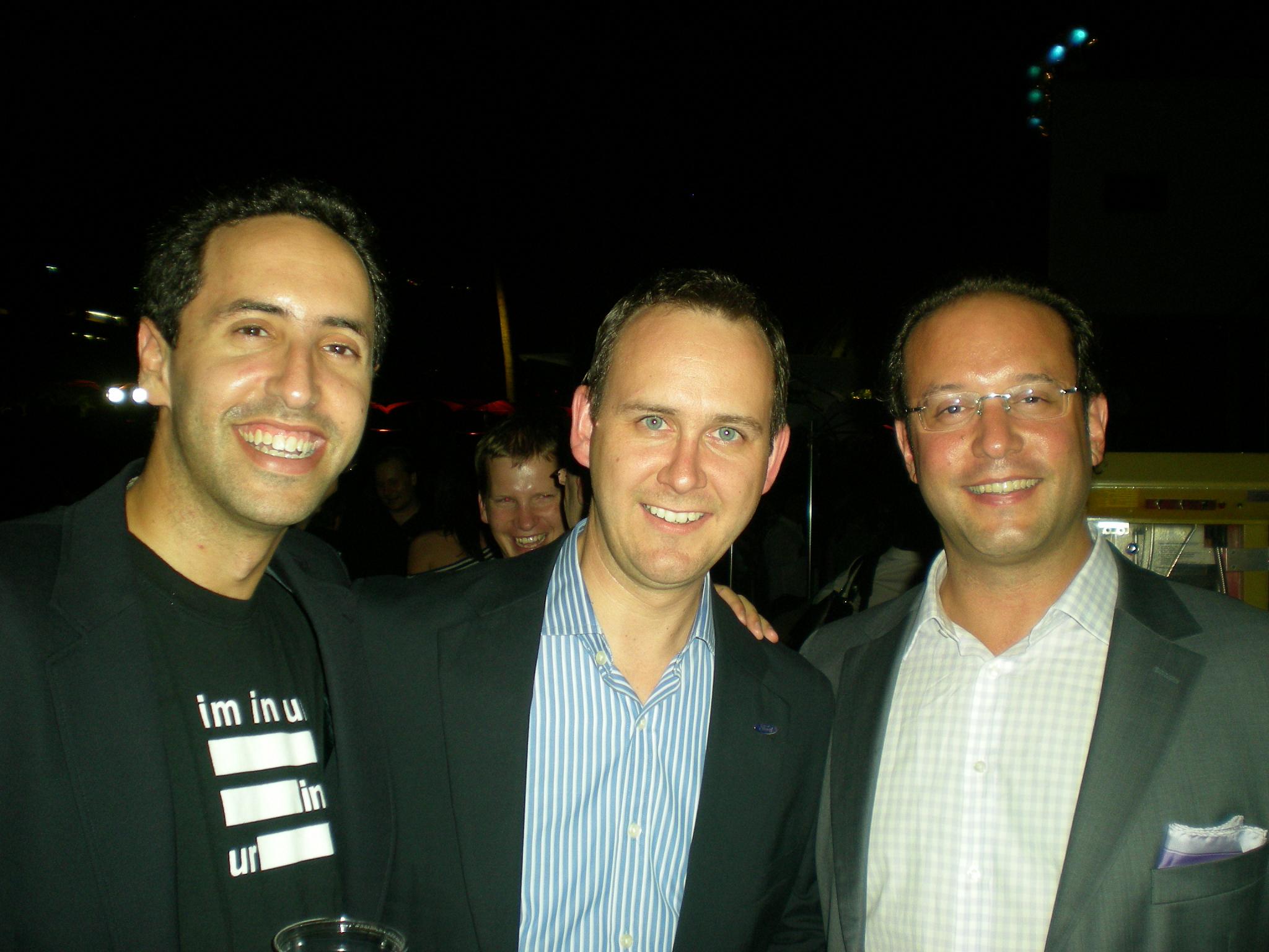 three men are smiling for the camera at night