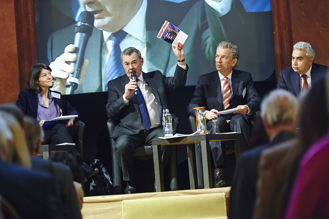four people are shown at an event during which a man is speaking and a woman holds up the newspaper