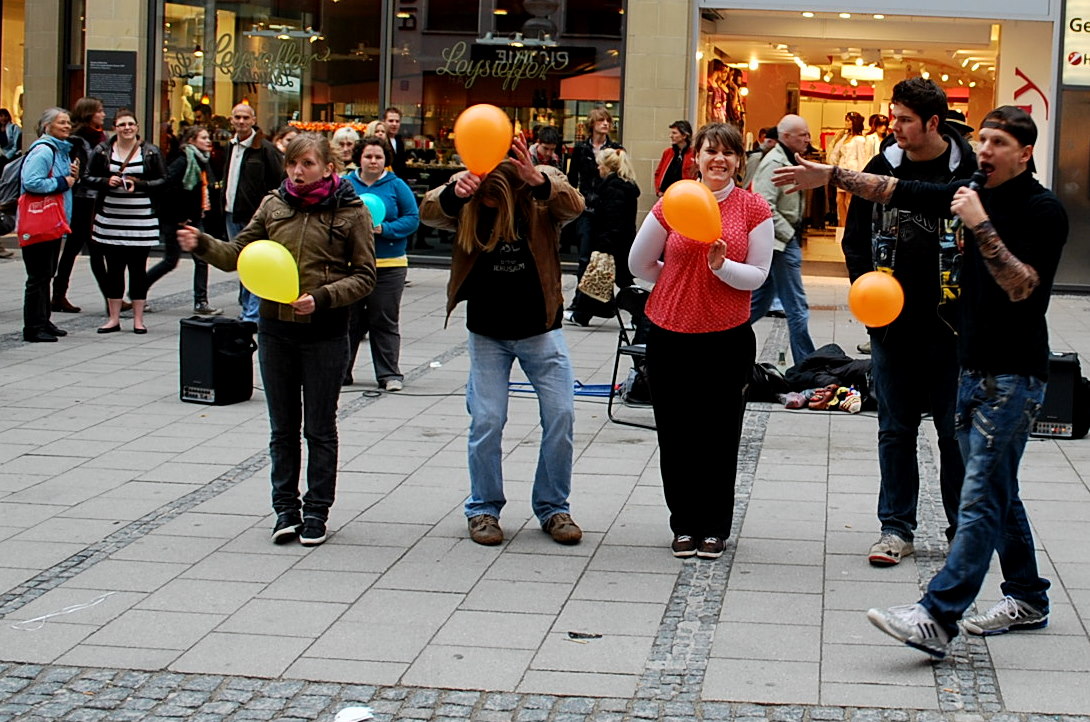 people walking on a sidewalk with orange and yellow balloons