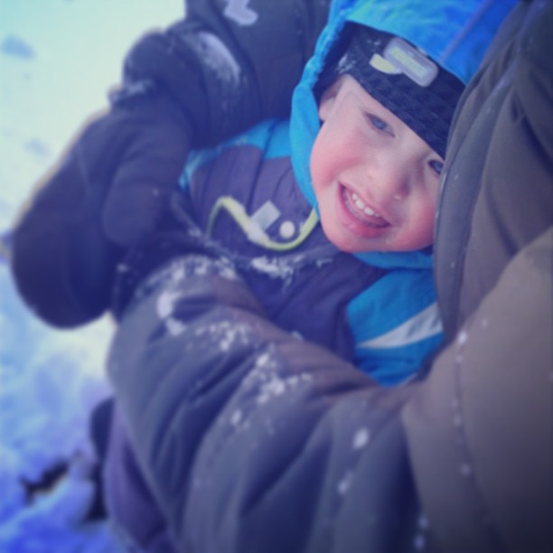 a smiling child wearing a blue jacket while sitting on a snowy surface