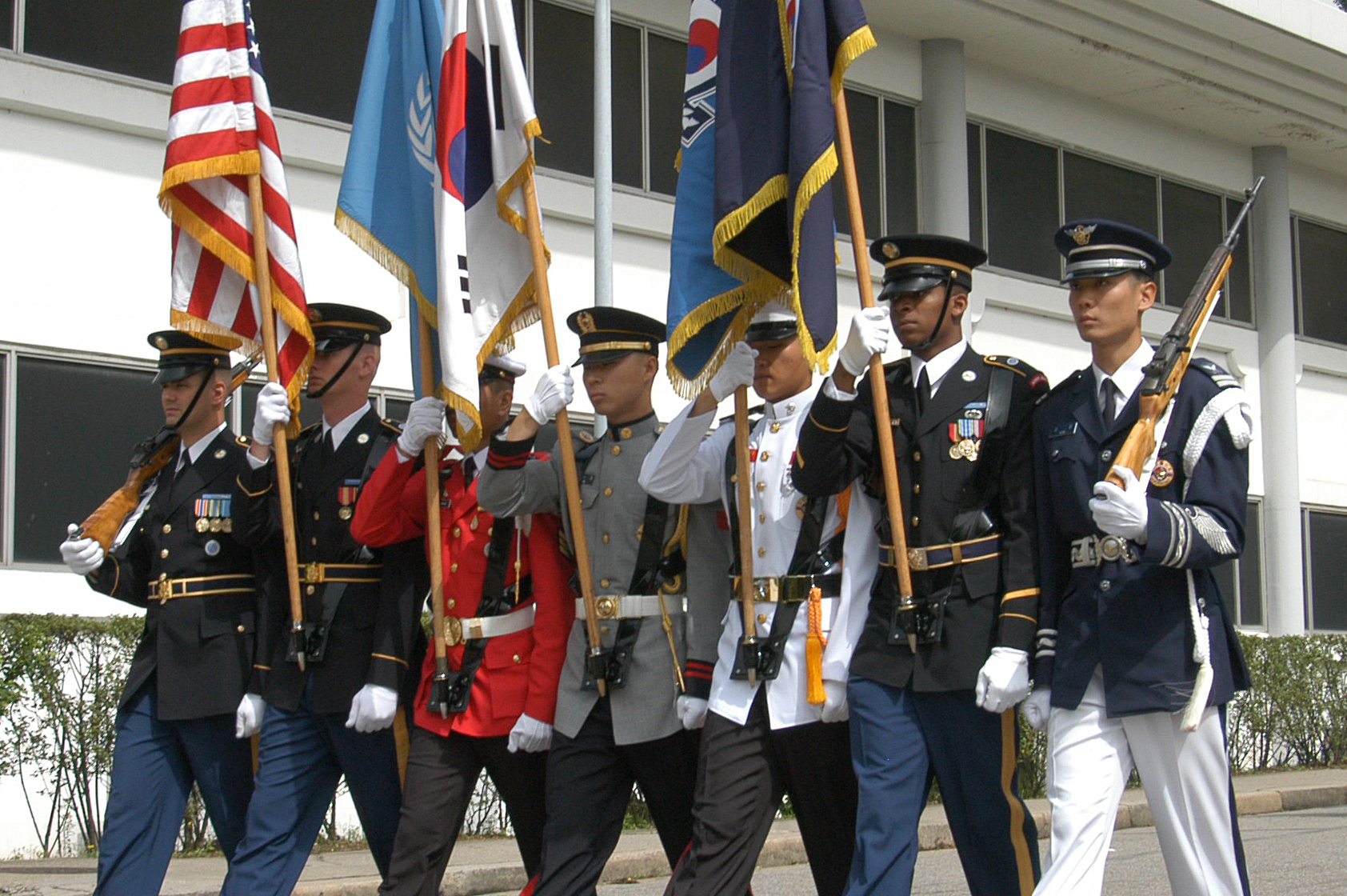 military men walk behind each other and hold flags