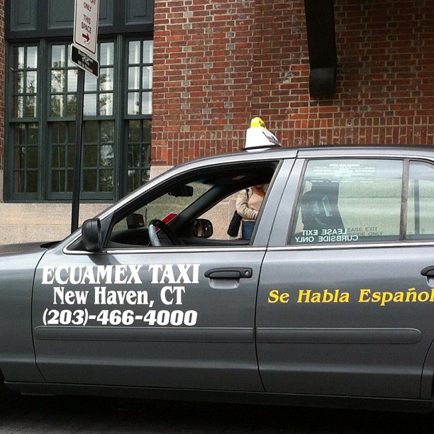 a silver taxi with a woman behind the driver's seat
