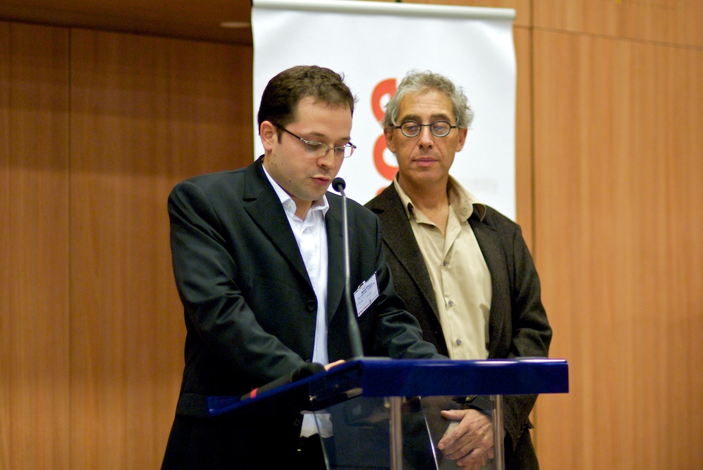 two men standing in front of a microphone in a conference room