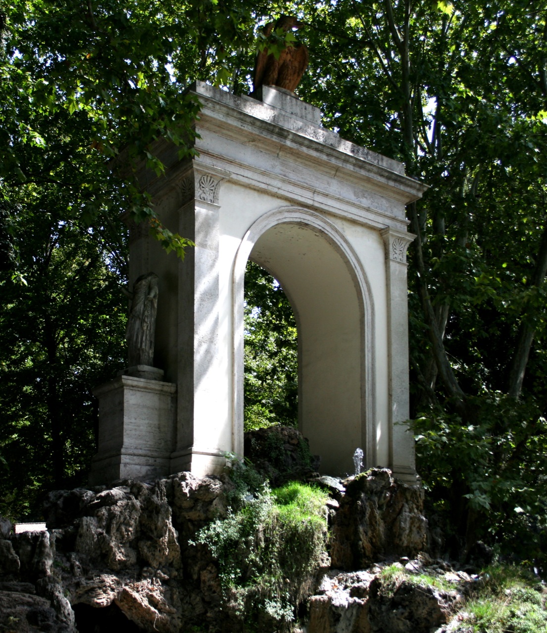 a stone arch over a waterfall with a statue under it