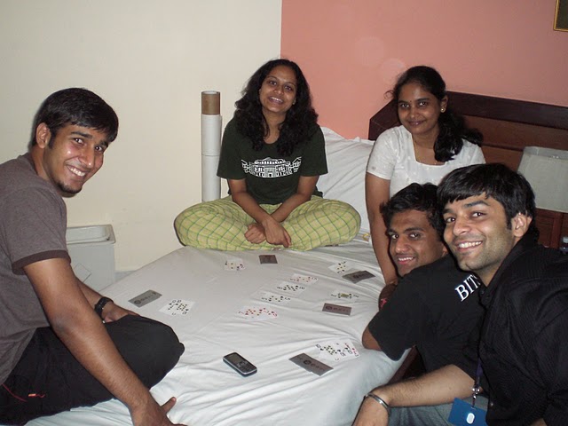 four people posing on a bed with cards spread out on it