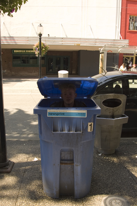 a man sitting in a blue bin on a street