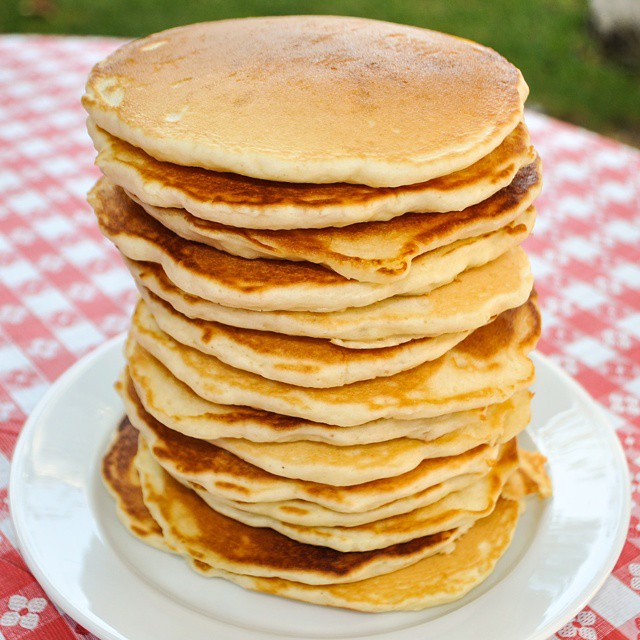 stacks of pancakes sit on a plate atop a red checkered tablecloth