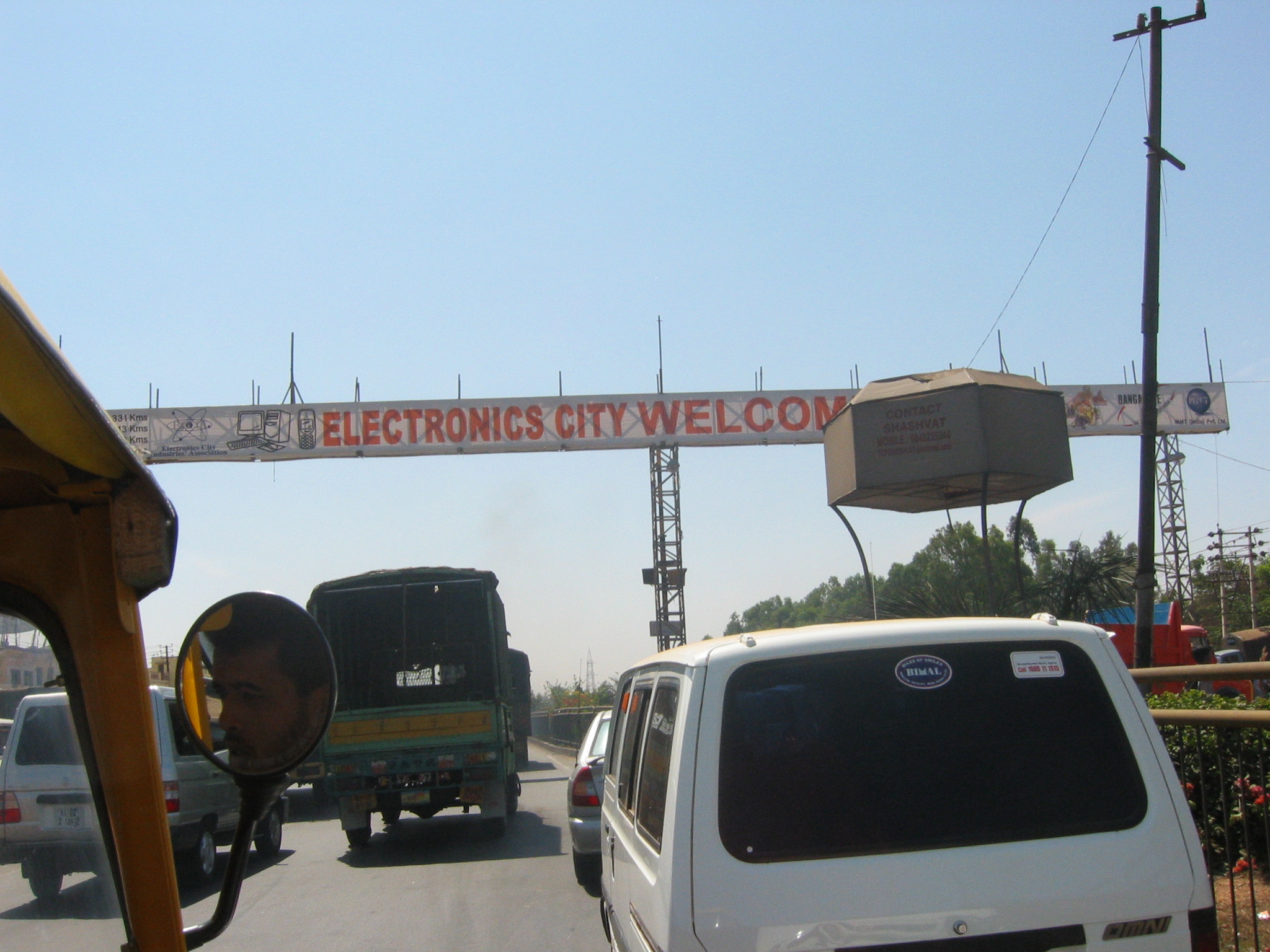 some cars driving down a road under an electronic city welcome sign
