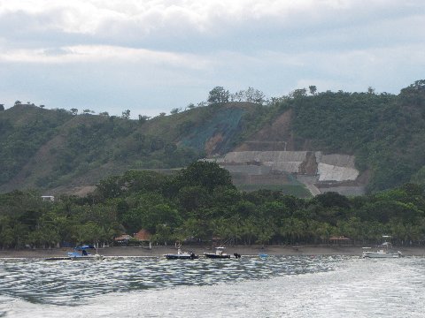 a beach with boats in the water and a hill behind