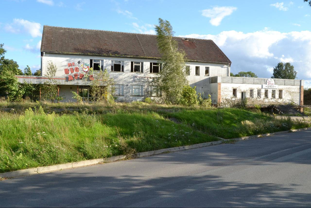 an abandoned building with graffiti and grass next to road
