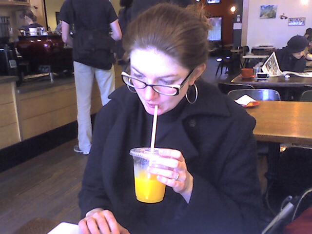 a woman drinking orange juice from a drink in a restaurant