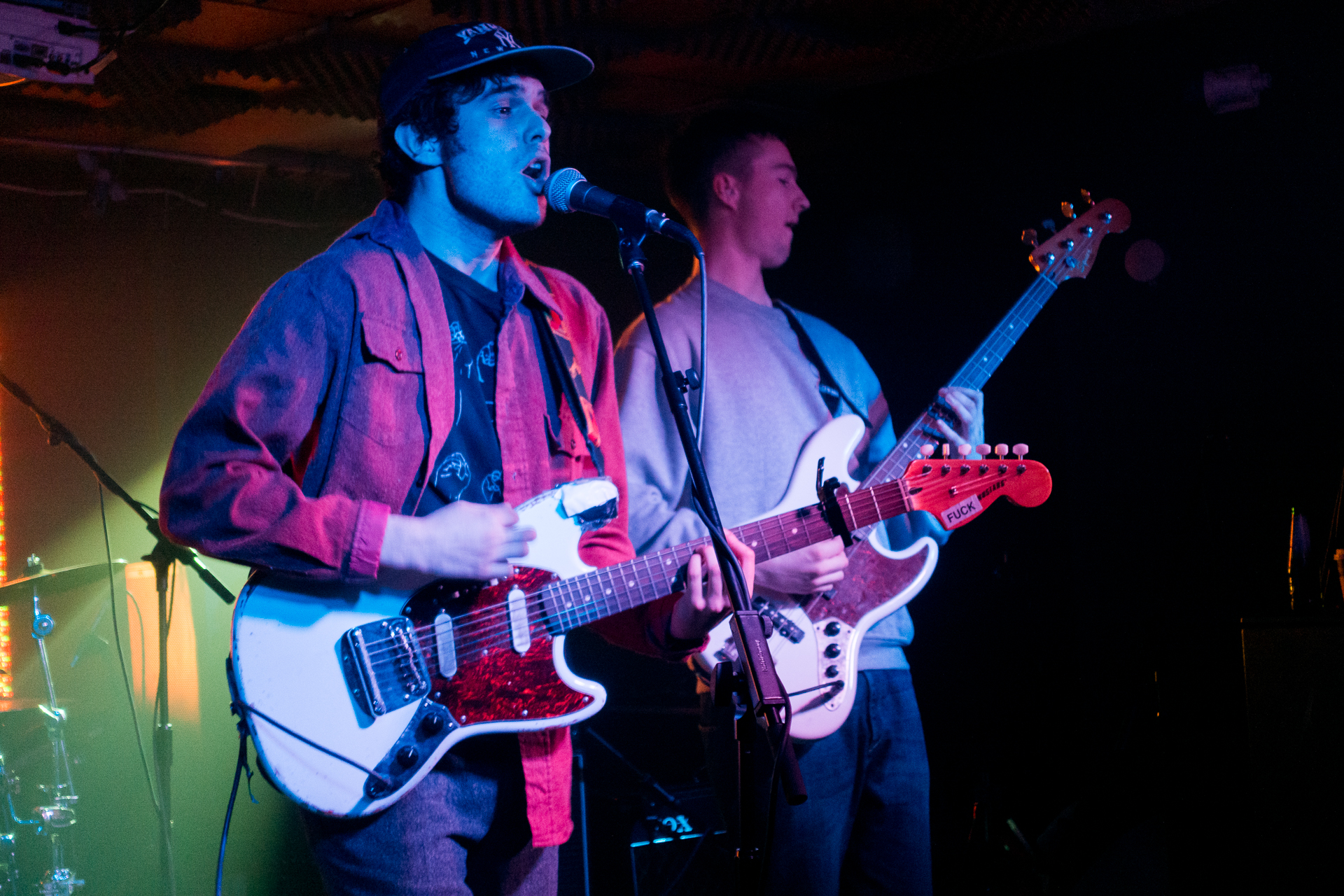 two men sing while playing guitars on stage