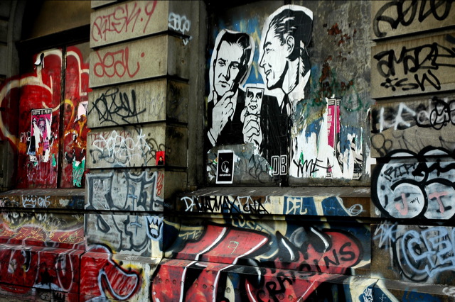 several grafitti on a building near by a wall with graffiti