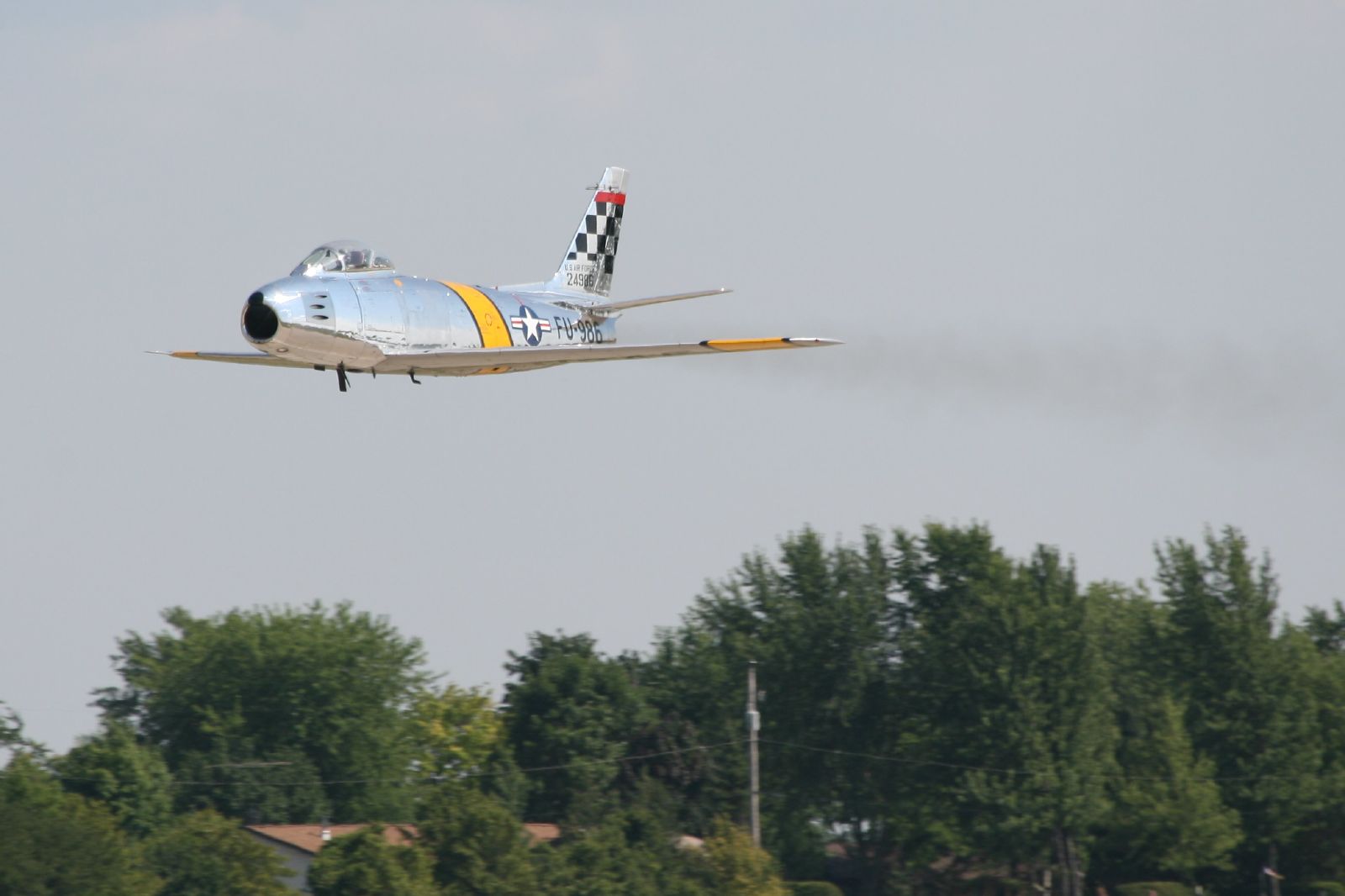 a silver airplane with checkered tail flying above a forest