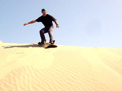 the man rides his board down the sand dunes