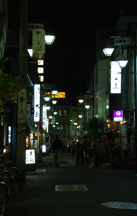 a narrow city street at night with many signs lit up