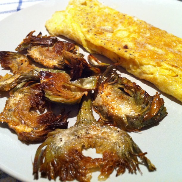 an omelet on a white plate, surrounded by fried onions and grilled artichoke