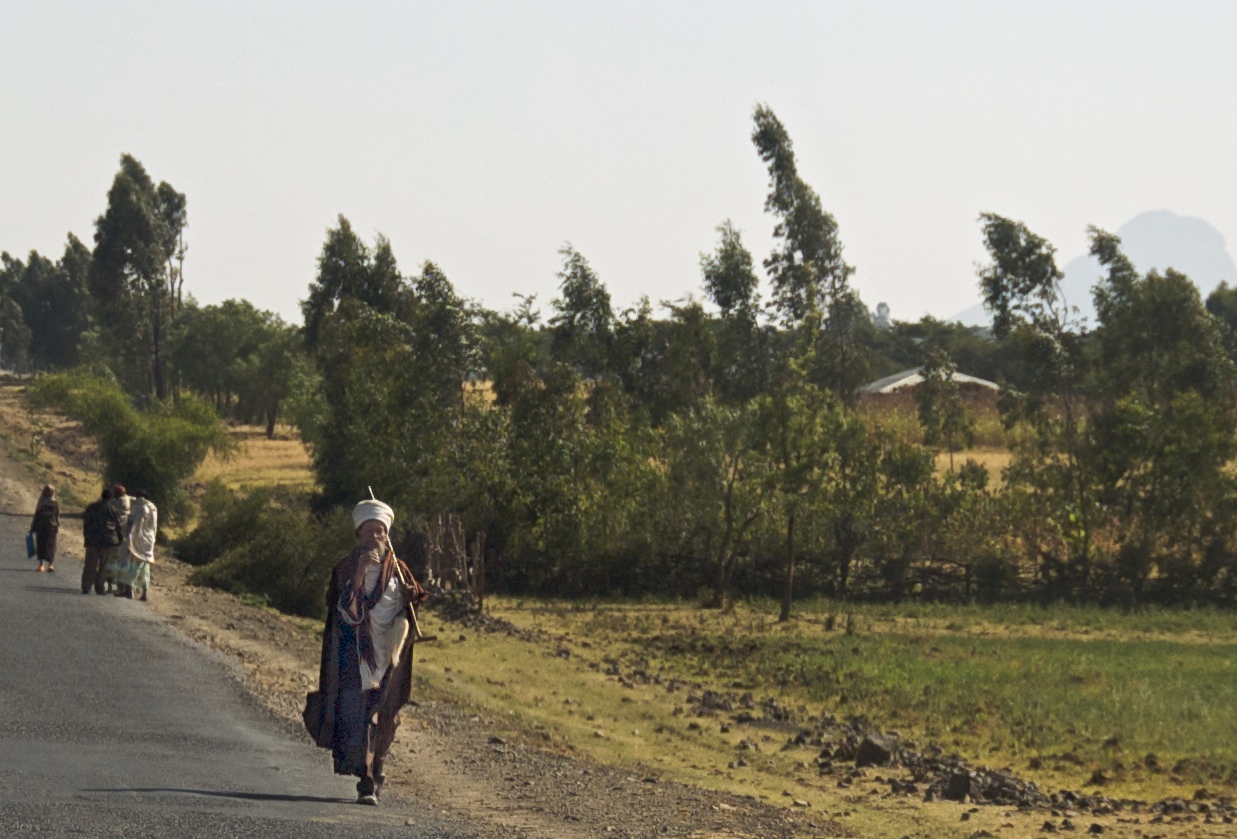 several people walk down a dirt road near a grass field