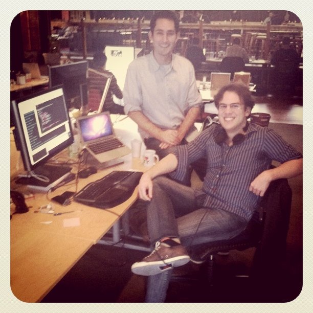 two guys sitting down smiling with their computers