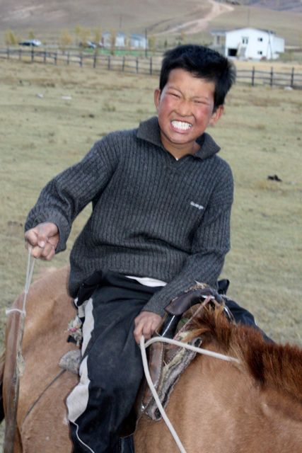an asian man riding a brown horse through the open plains