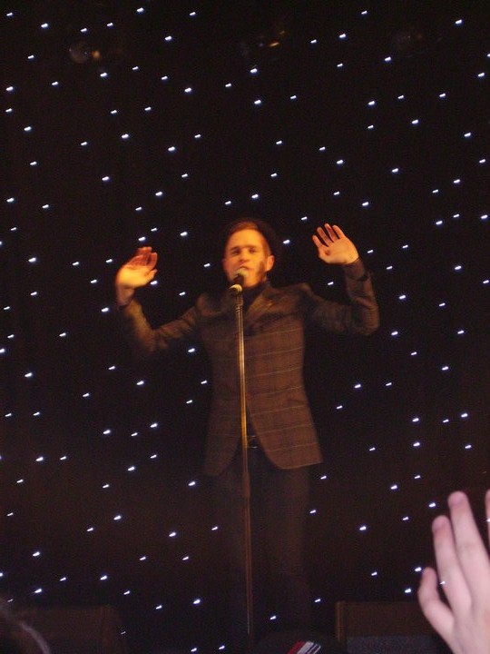 a male in a black jacket a microphone and lights