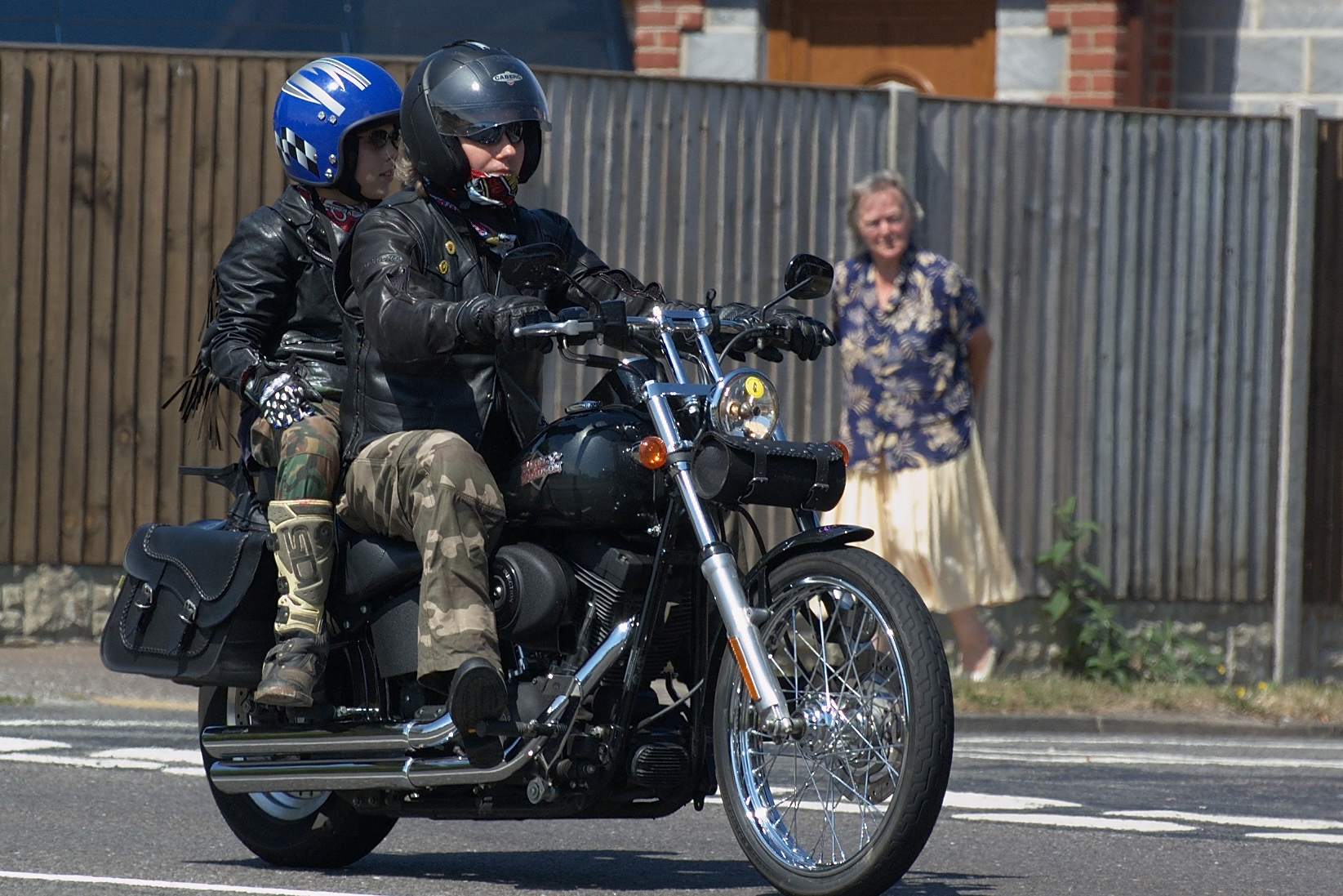 two people riding on the back of a motorcycle down a street