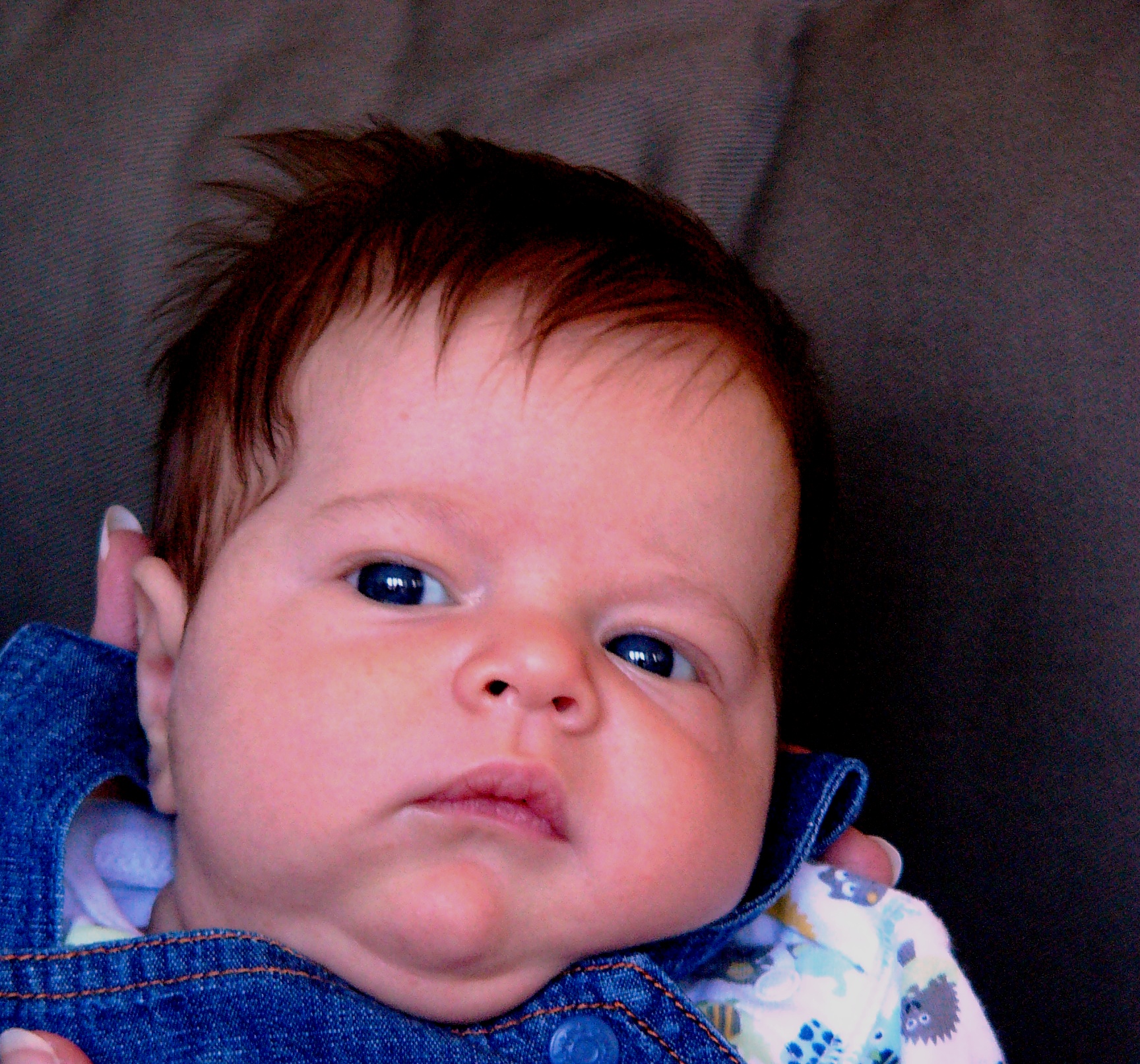 a baby is looking up and wearing a blue jean jacket