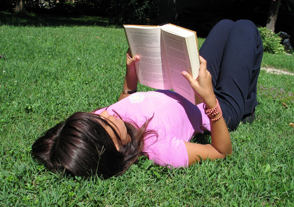 the woman is lying on the grass reading the book