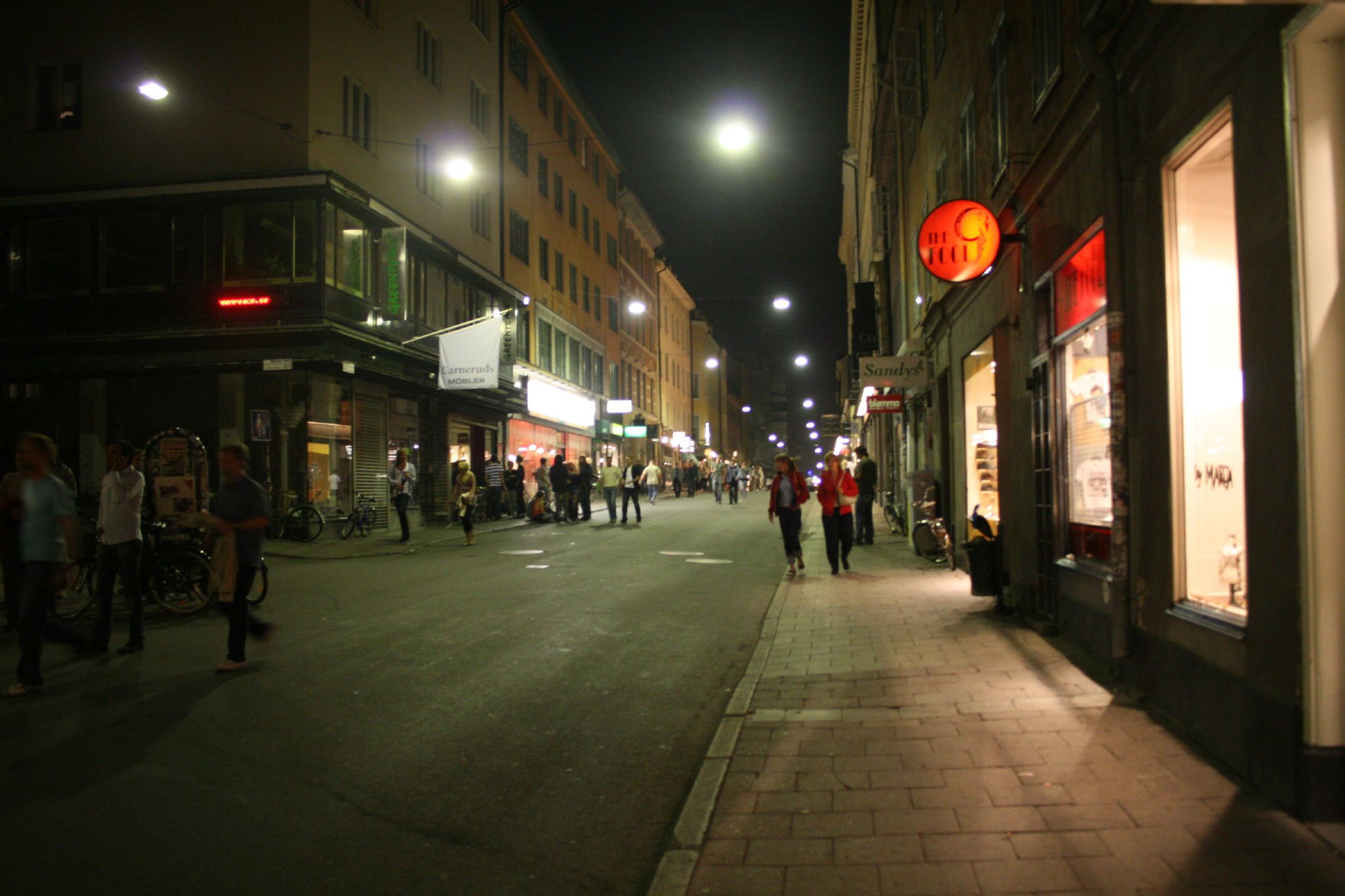 people walk down the street at night near stores