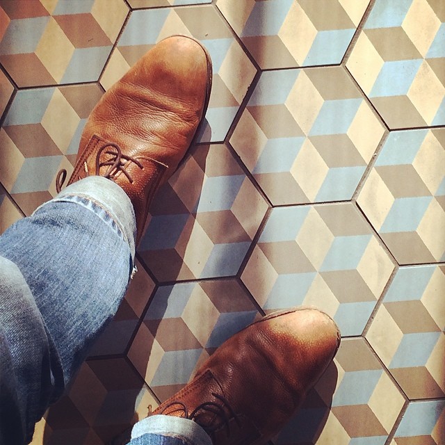 a man standing next to a pair of brown shoes on a checkered floor