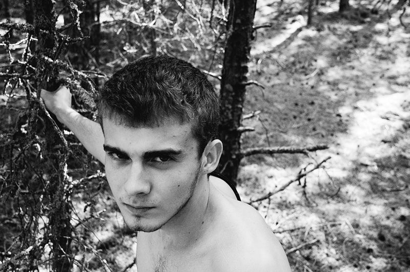shirtless young man leaning against trees in woods