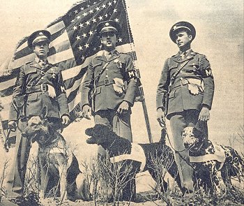two men in uniforms standing beside an american flag