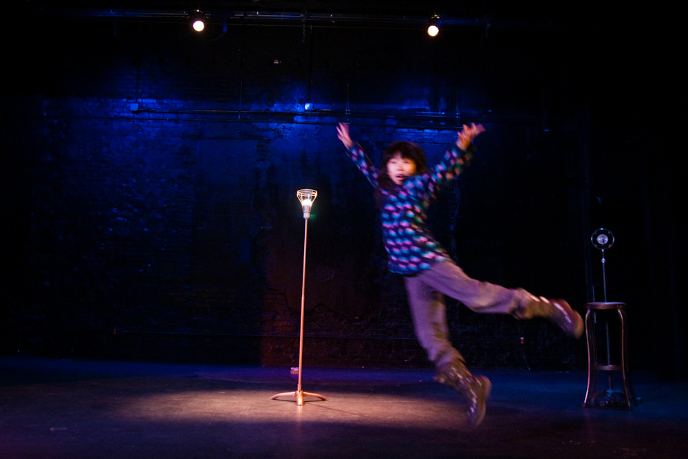 the man is standing in the air by the microphone and wearing jeans