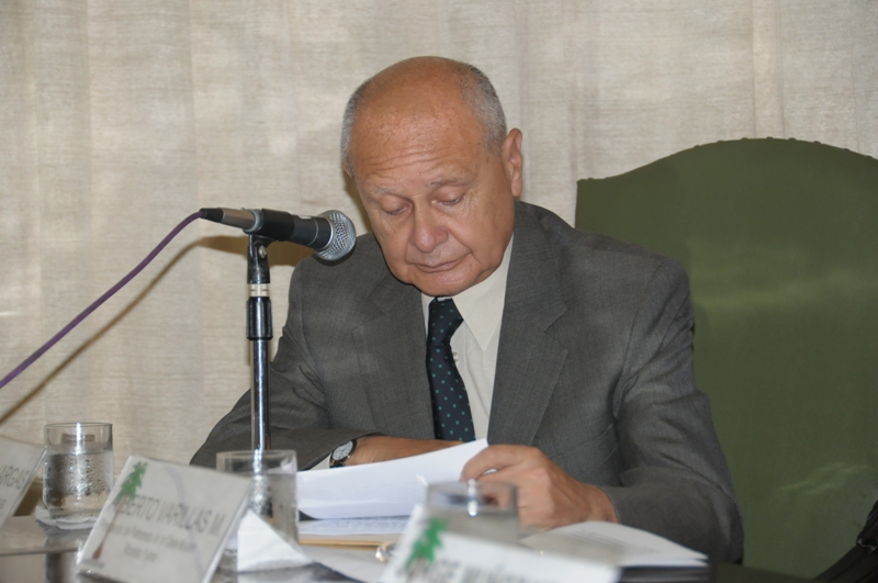 a man in a suit and tie sits at a table with papers and a microphone