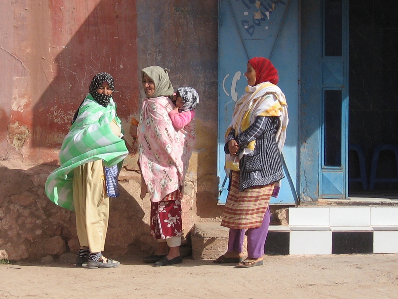 three woman with colorful clothes and scarves looking at another woman in a pink scarf