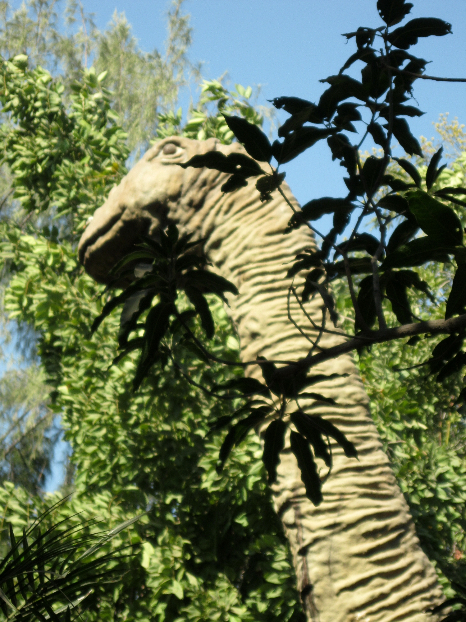 a toy dinosaur in a forest with green trees