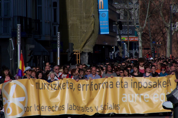 large crowd in front of sign on street with flag