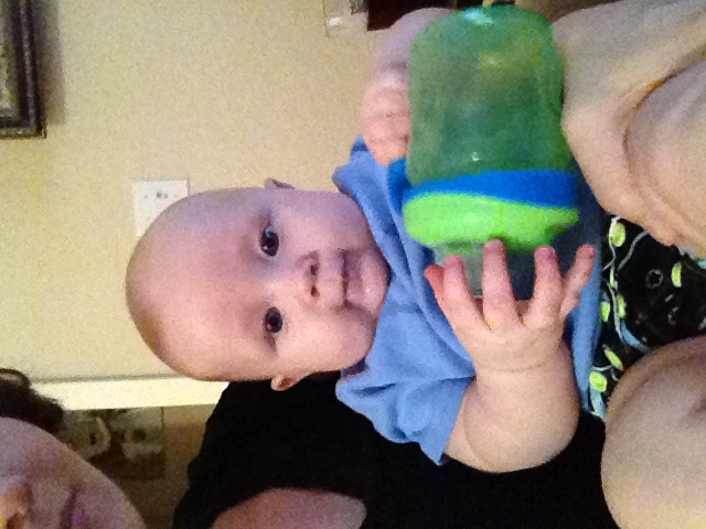 a baby drinking out of a green cup and holding another baby