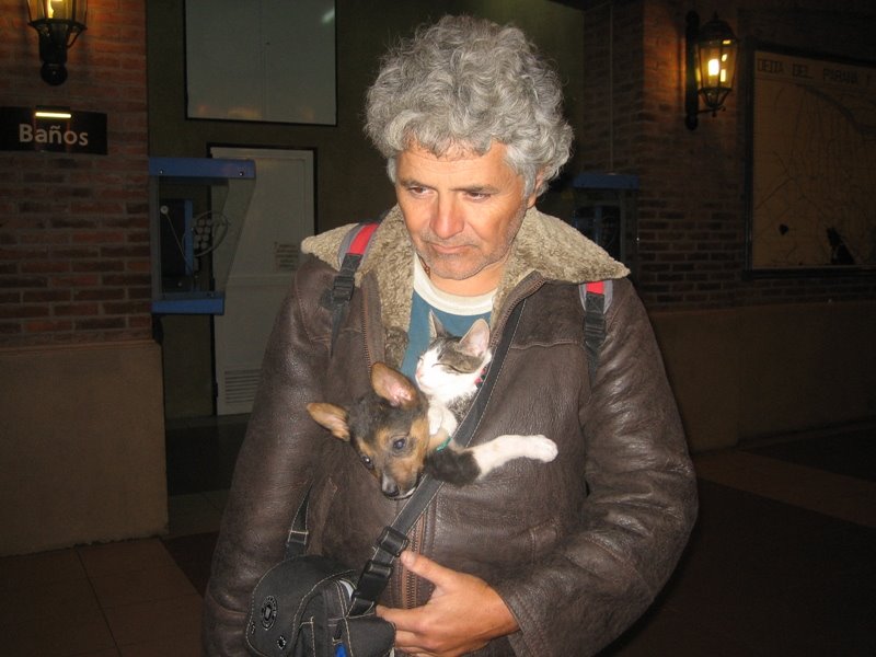 a man in a coat holding a small dog and cat