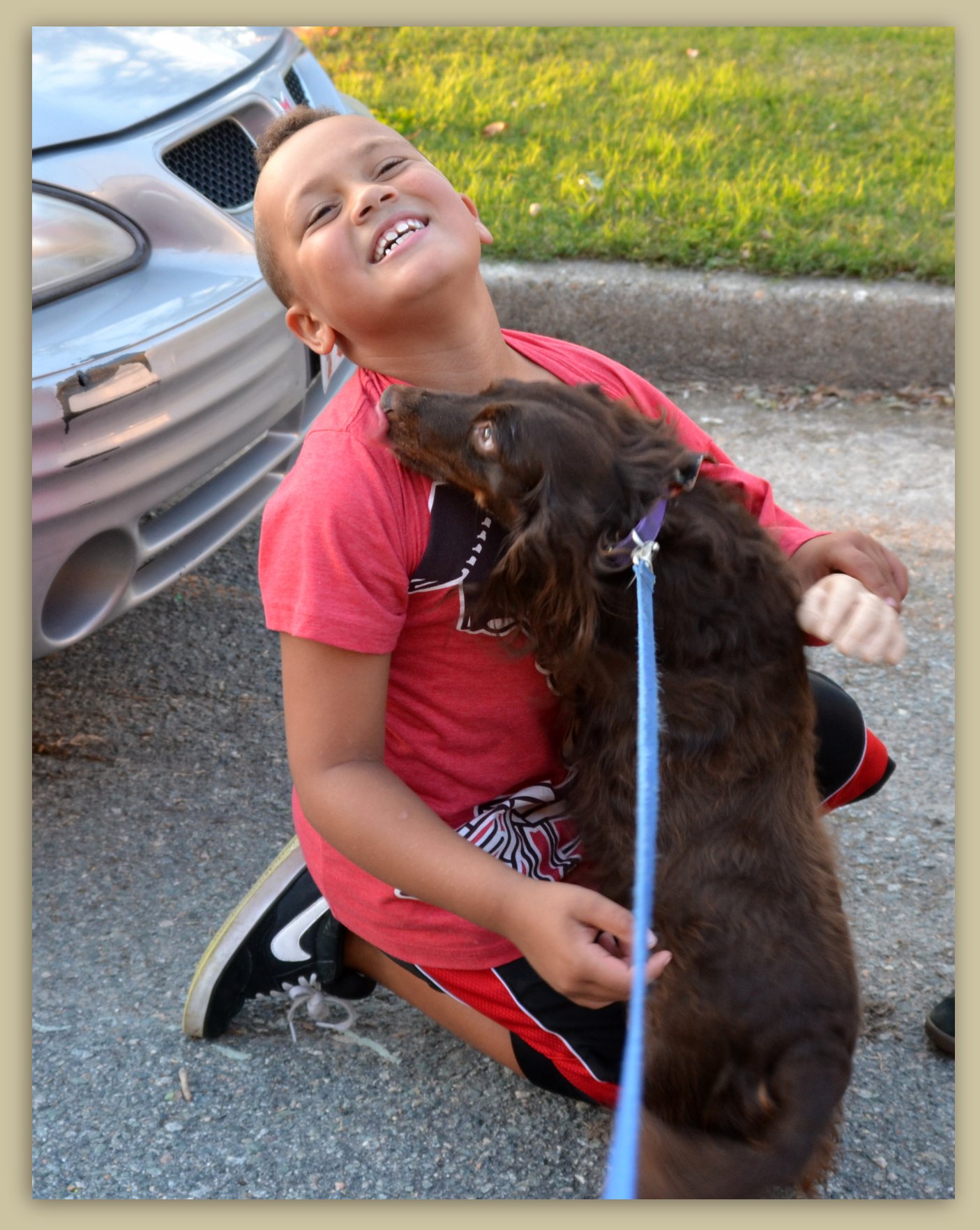 the boy smiles as he sits by the car with his puppy