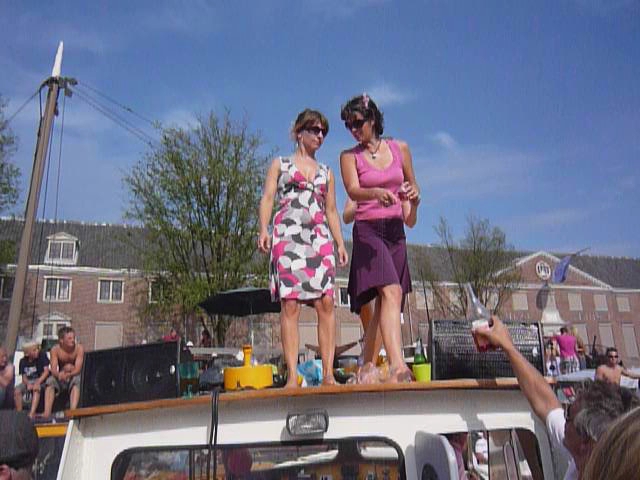 two women in pink dresses standing on the roof of a boat