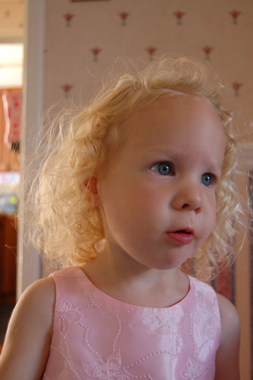 a little girl with curly blonde hair is posing for the camera