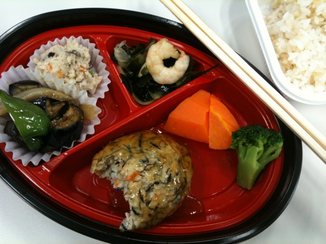 a plate of food including sushi, vegetables and a bowl of rice
