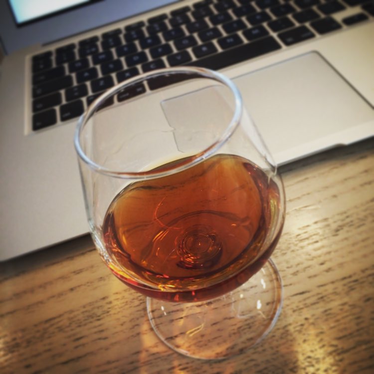 a glass sitting on top of a wooden table next to a laptop computer