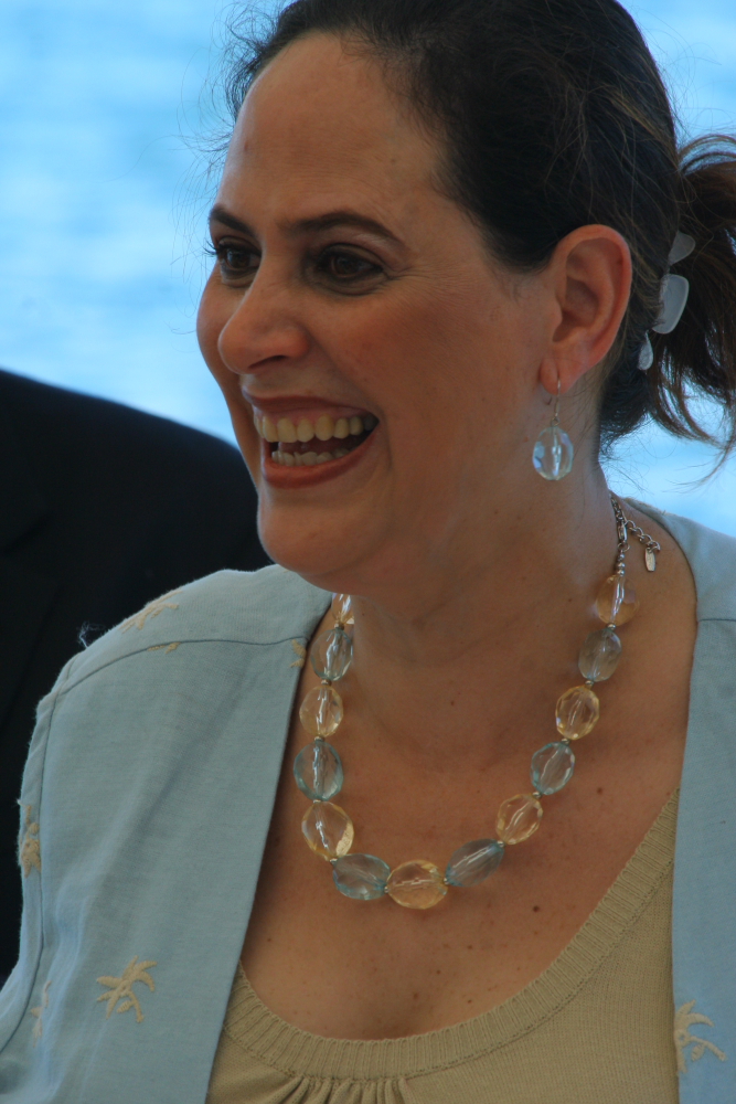 a smiling lady wearing a light blue blazer and matching earrings