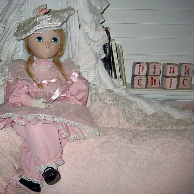 a doll sitting on a bed with a pink dress and bonnet