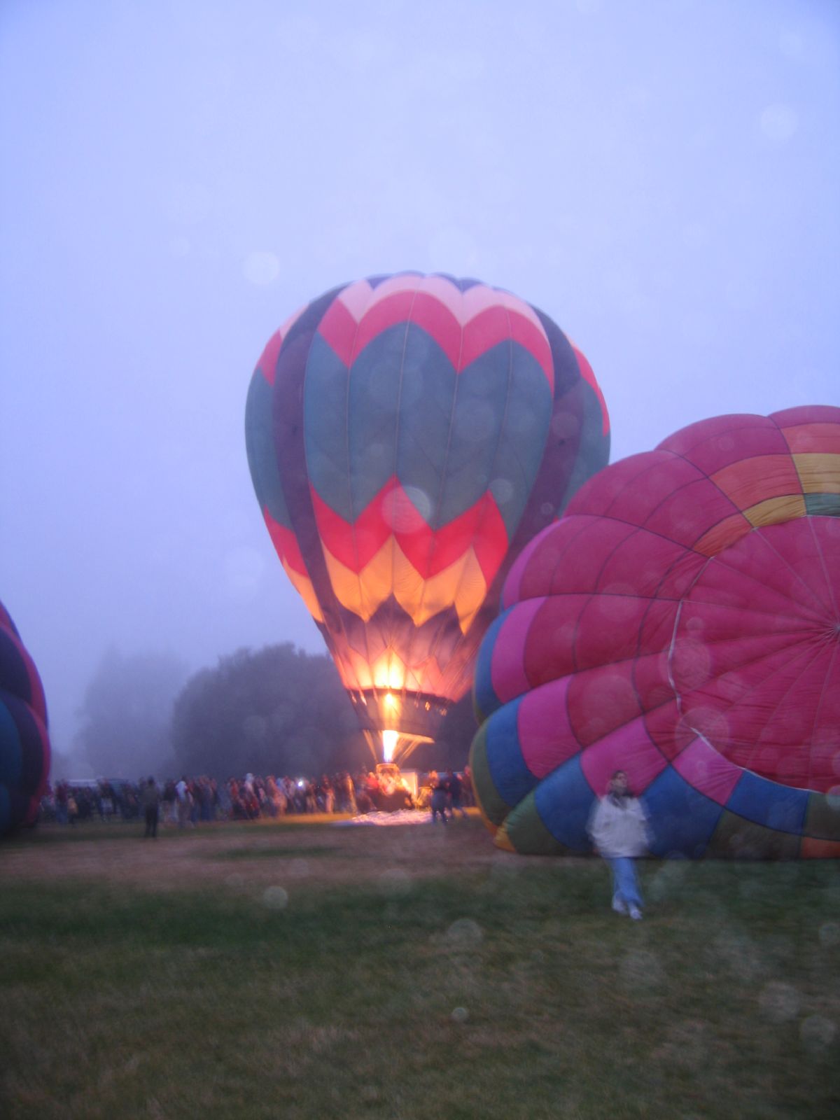 a group of  air balloons in the sky with a fire burning in the distance