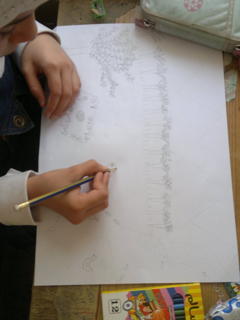 young child writing on a piece of paper with crayons on the top