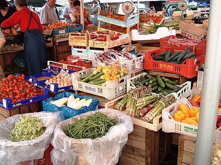 people walking around an outdoor market with vegetables